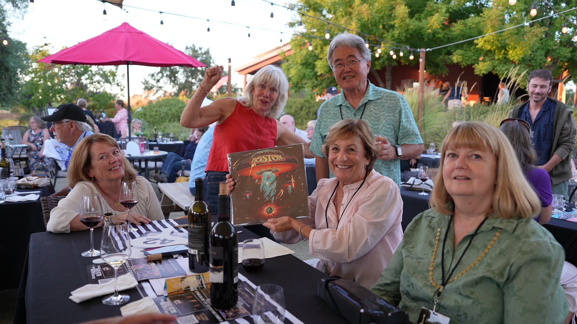 Smiling guests at a Harmony & Healing benefit concert hold up a BOSTON album.