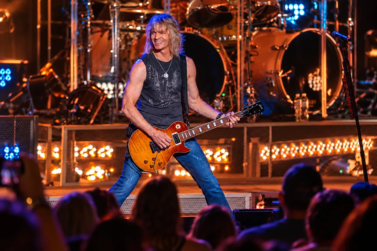David Victor, founder of Harmony & Healing, smiling on stage with a sunburst Les Paul guitar on tour with BOSTON in 2014.