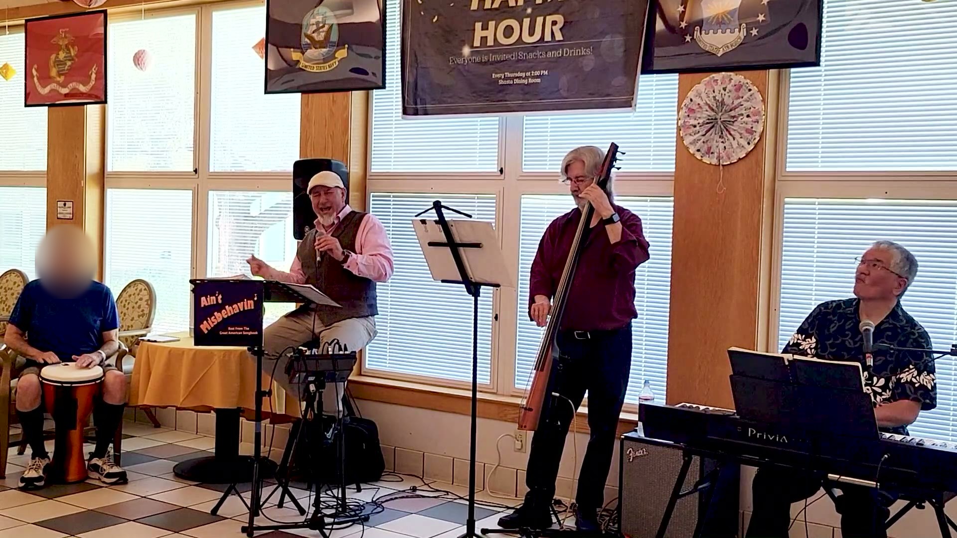 A jazz combo with keys, upright bass and a singer plays at a VA Happy Hour while a patient plays a hand drum with them.